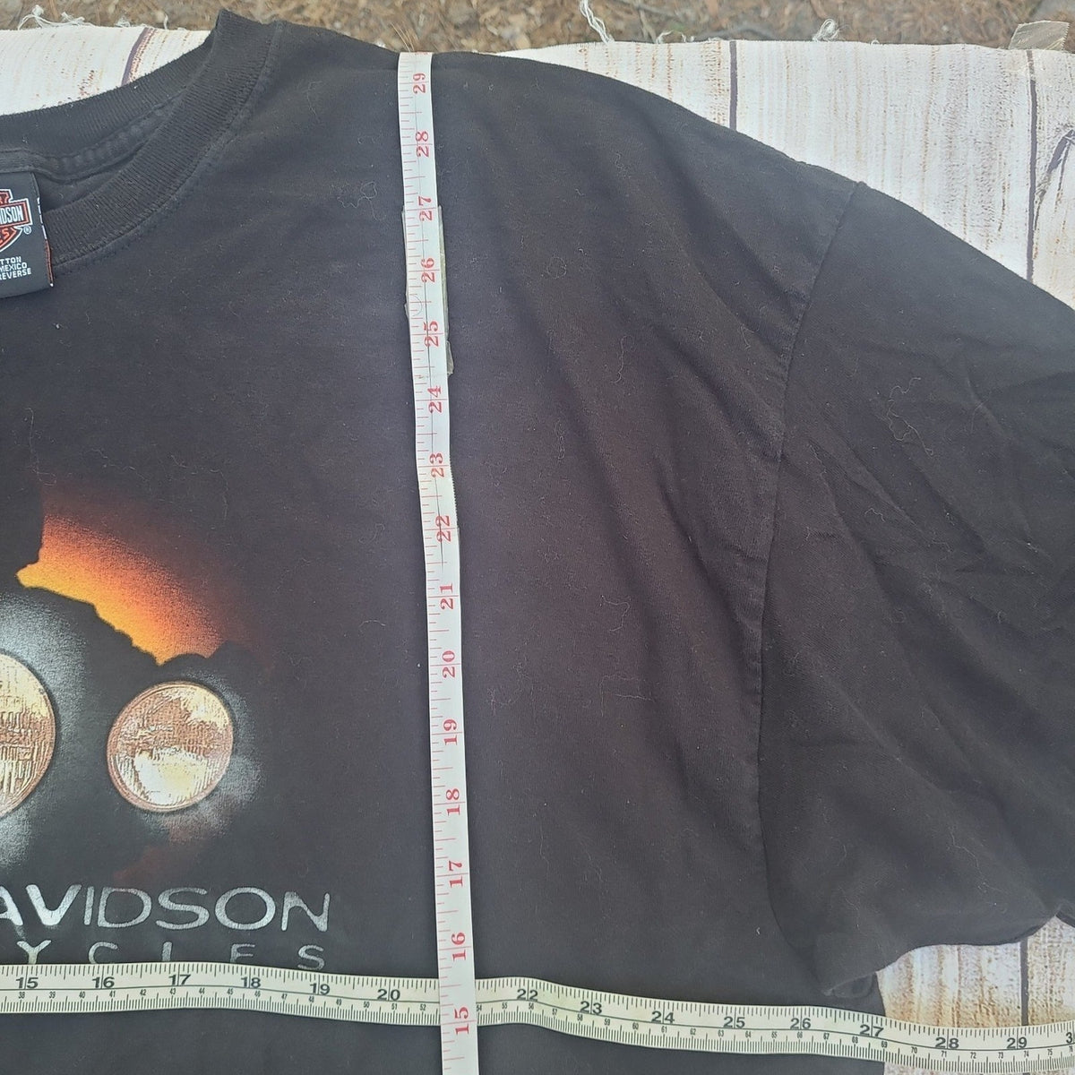 Black vintage Harley Davidson shirt with motorcycle headlight graphic laid flat with measuring tape