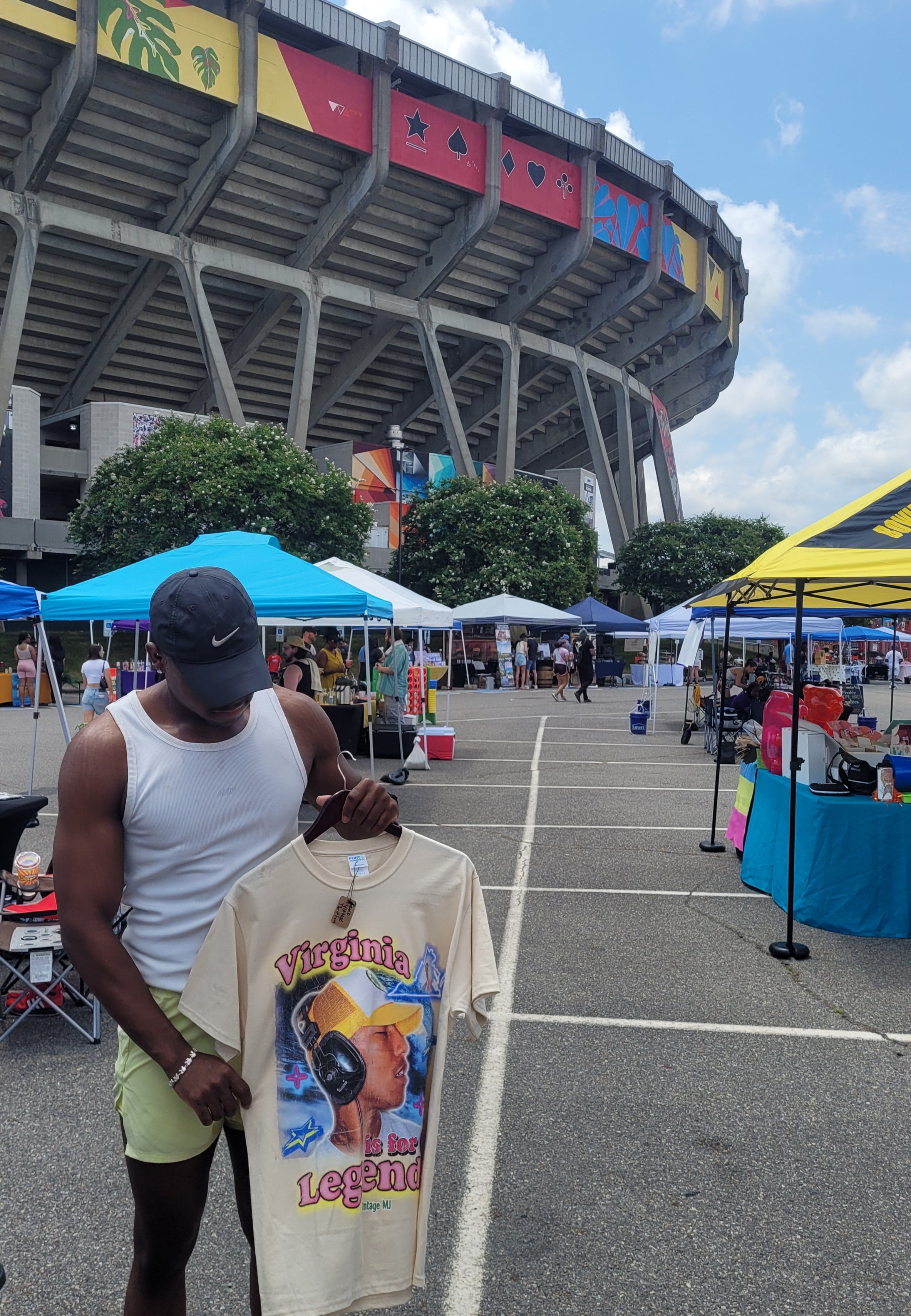 Man holding a large virginia legends shirt with a colorful design in front of a stadium.