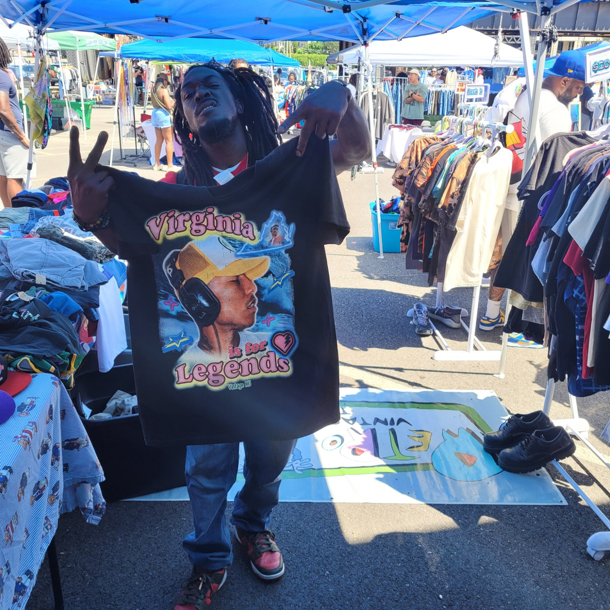 Person holding black Virginia Is for Legends Y2k P tee with colorful graphic at outdoor market